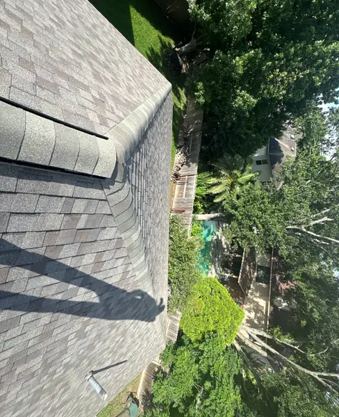 Steep roof slope with fresh laminate shingles over a tree-lined yard in Houston