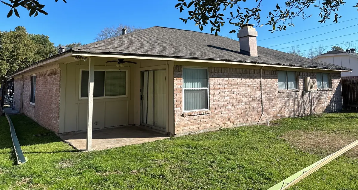Rear of a one-story brick Katy home with a new tan-brown roof and patio
